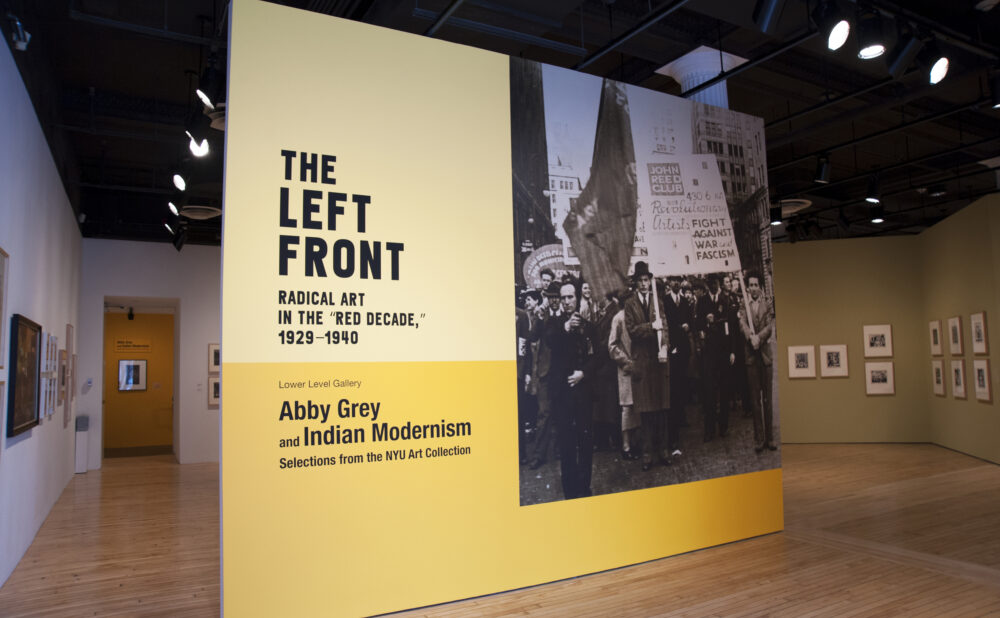 The entrance wall of an exhibition titled "THE LEFT FRONT", featuring yellow and black wall panels with large introductory graphics and photos. Alt text generated by AI