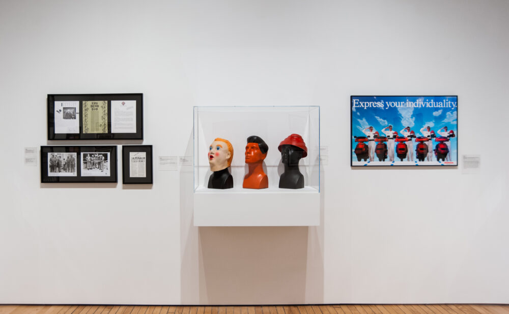 Clean white wall section featuring a white shelf holding small sculpted heads, flanked by framed artworks. (Alt-text generated by AI)