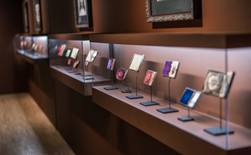 Close-up view looking down an illuminated vitrine display containing small mounted artworks. (Alt-text generated by AI)