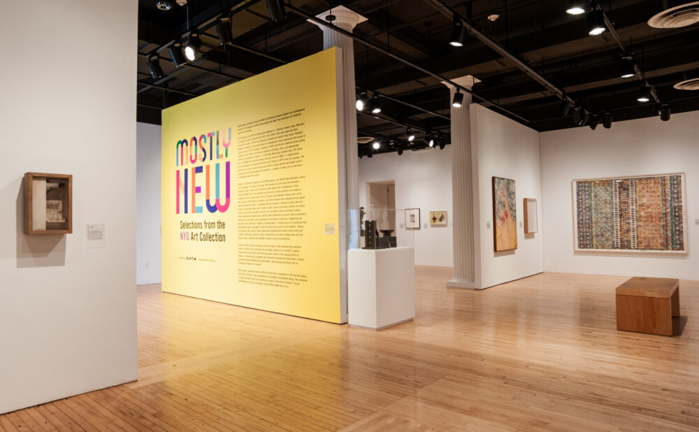 Art gallery with a yellow wall displaying "MOSTLY NEW" exhibition title and various artworks on white walls.