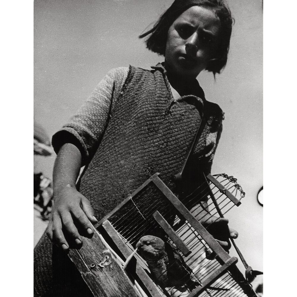 Black-and-white portrait of a young boy looking into the camera while holding an object across his chest. (Alt-text generated by AI)