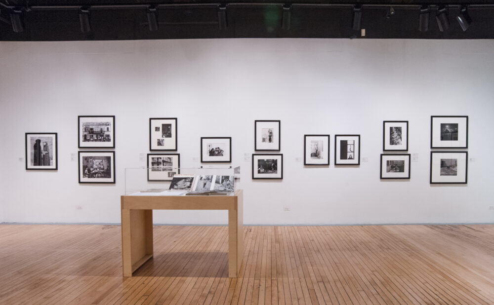 Straight-on view of a gallery wall lined with framed photos and a small wooden display case in front. (Alt-text generated by AI)