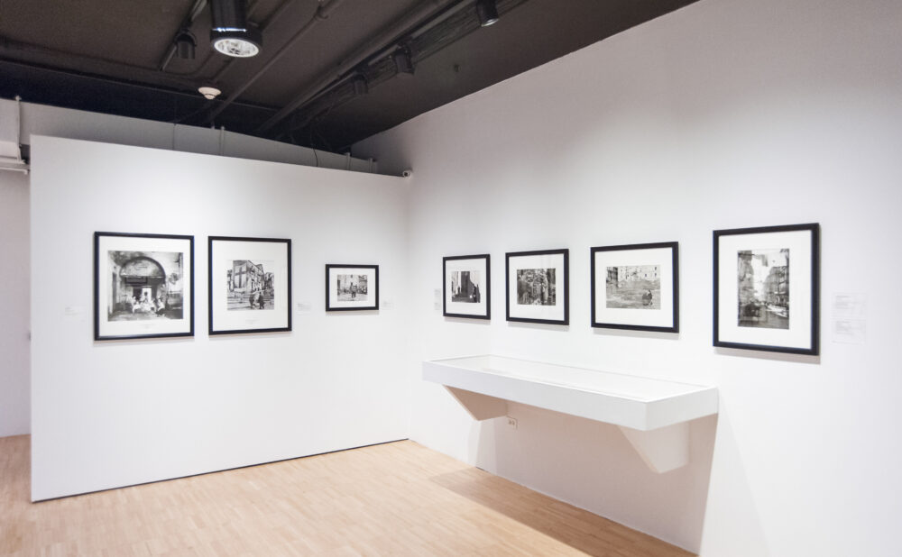 Exhibition corner displaying framed photos on white walls above a low white display ledge. (Alt-text generated by AI)
