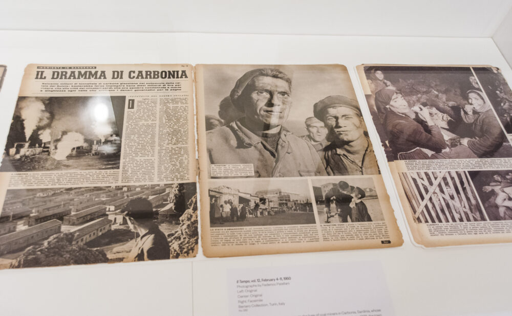 Close-up view of open archival publications and photojournalism articles laid flat inside a display case. (Alt-text generated by AI)