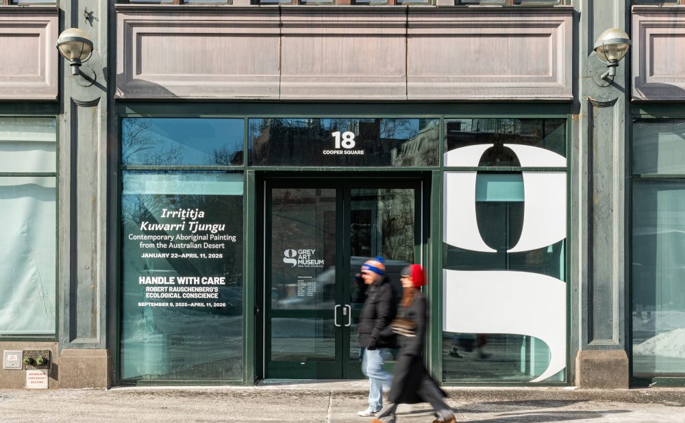 Entrance of Grey Art Museum at 18 Cooper Square, featuring exhibition advertisements and pedestrians walking by.