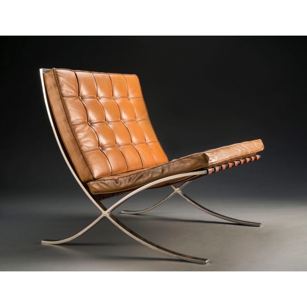 Ludwig Mies van der Rohe Barcelona chair with tan button-tufted leather cushions on a curved chrome X-frame. (Alt-text generated by AI)