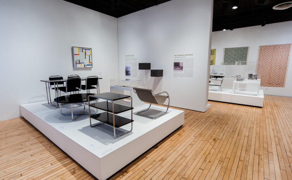 Angle view of a raised display platform showcasing modern seating and glass shelving units inside a spacious exhibition hall. (Alt-text generated by AI)