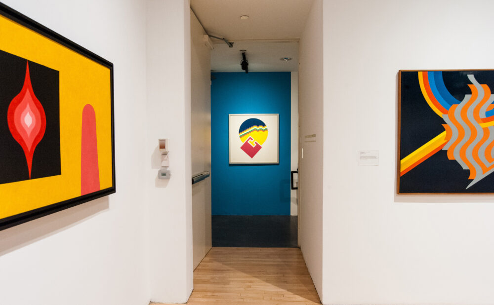 A gallery with abstract paintings on white walls and a wooden floor.