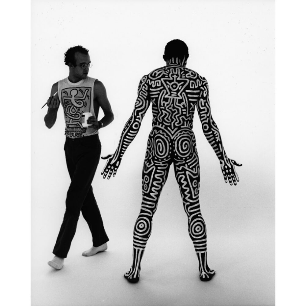 Studio photograph depicting Bill T. Jones and Keith Haring posing against a plain background, with Bill nude and decorated with body paint. (Alt-text generated by AI)