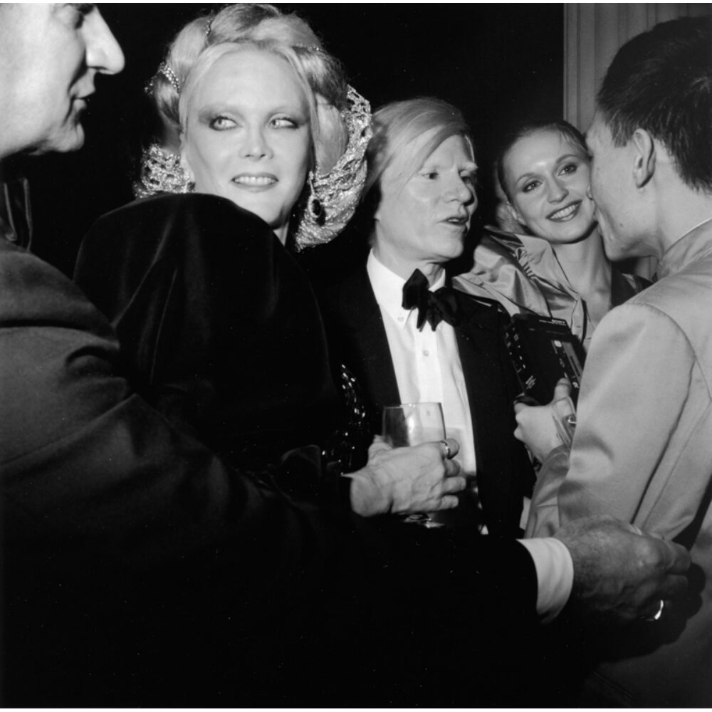 Black-and-white party photograph capturing Andy Warhol and guests at a formal event. (Alt-text generated by AI)