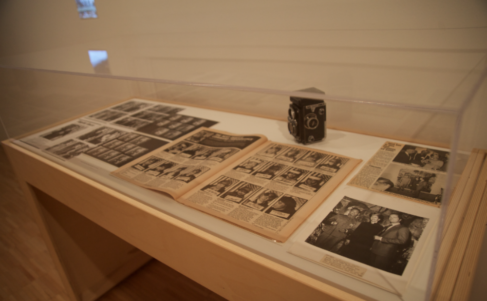 Wooden display vitrine containing archival documents and photographs. (Alt-text generated by AI)