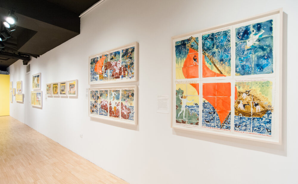 Perspective view along a white gallery wall featuring several large framed grid-style artworks. (Alt-text generated by AI)