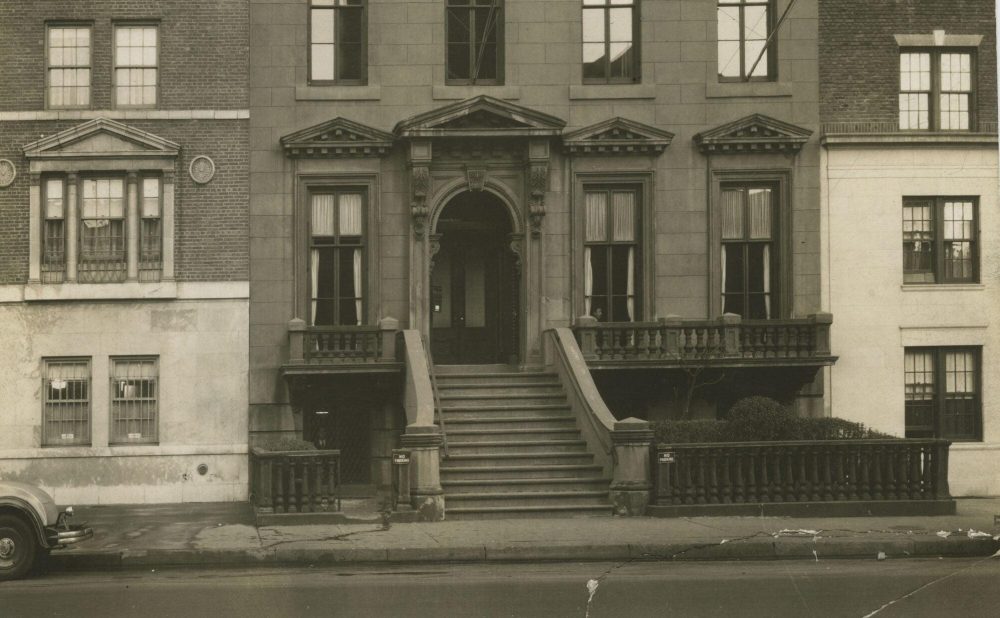 Front facade of a historical townhouse with stone staircase and arched entrance, flanked by red brick sections and decorative windows. Alt-text generated by AI. Transcribed Text:  "No Parking." "No Parking."