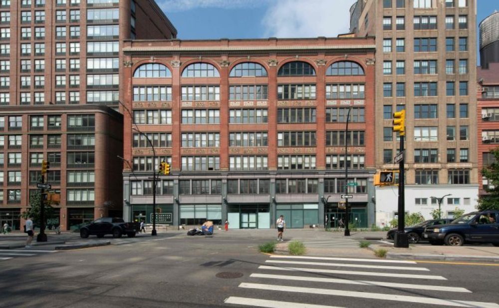 A red-brick building with arched windows centered in a city street scene, flanked by taller buildings.