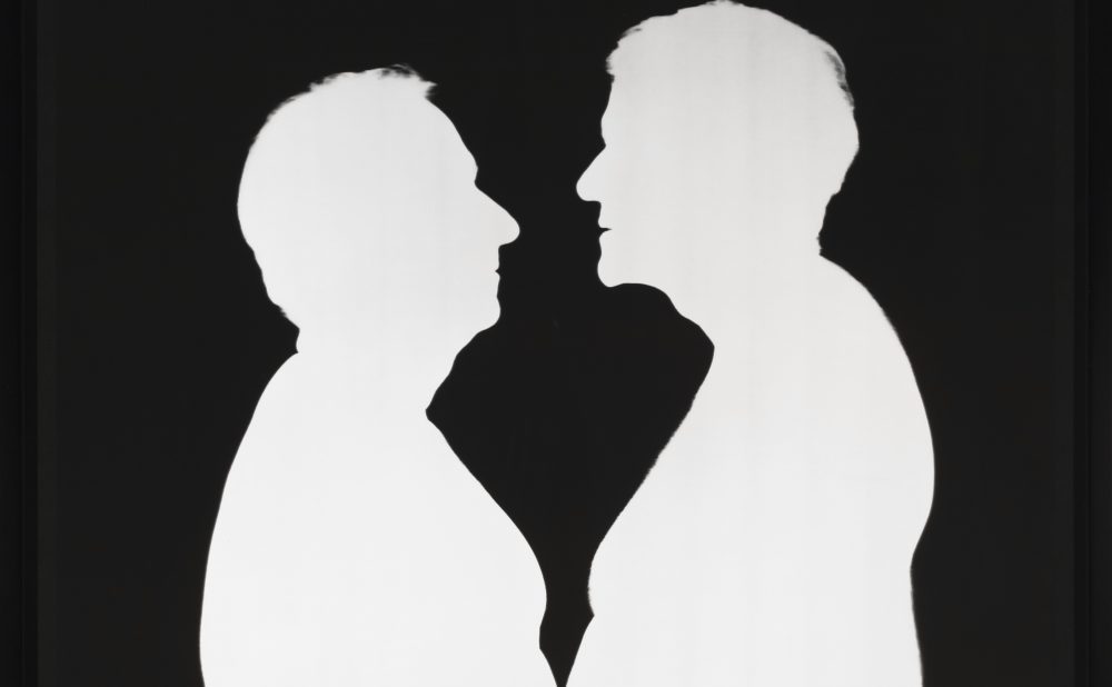 Two men face each other in stark silhouette. The men are white and the background is black. The contrast is sharp like a Victorian silhouette and flattens the figures, who are close enough that their possibly bare bellies possibly touch.
