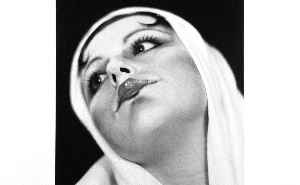 Black and white artwork of a person with a draped fabric headscarf, gazing upwards. Alt-text generated by AI.