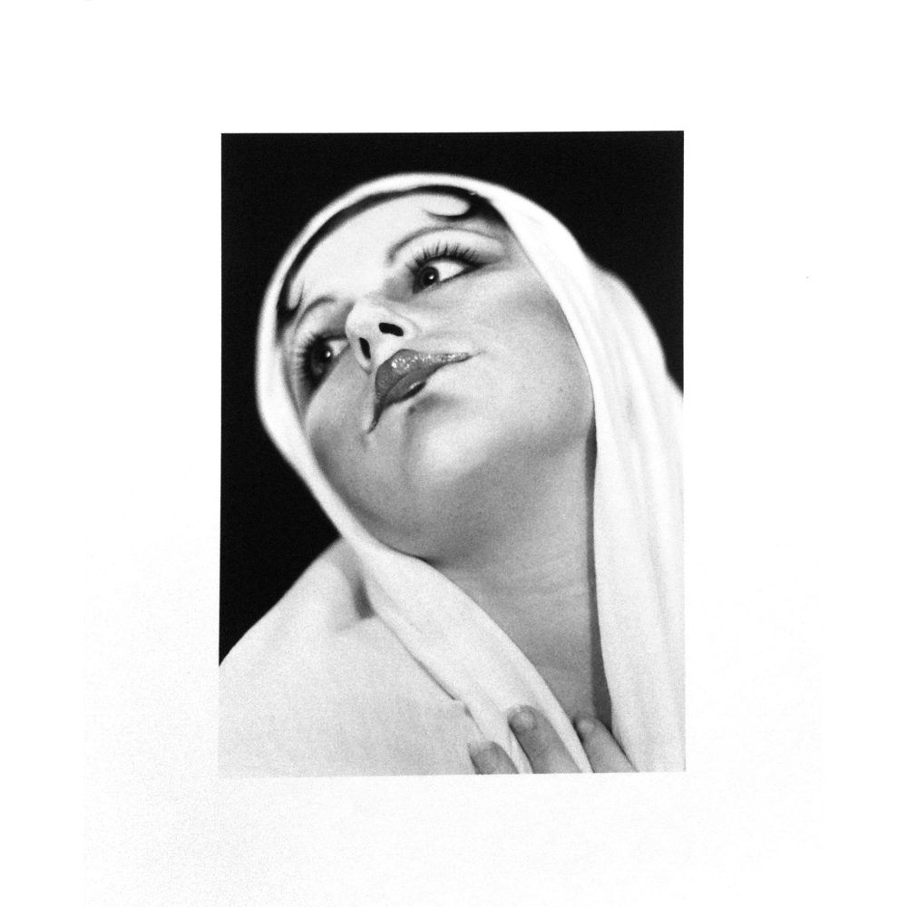 Black and white artwork of a person with a draped fabric headscarf, gazing upwards. Alt-text generated by AI.