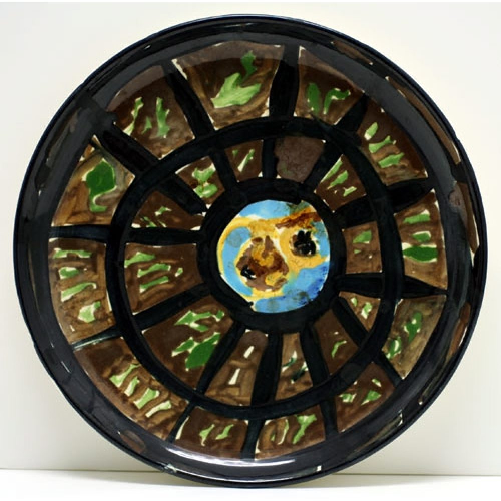 Ceramic plate with abstract design featuring a central yellow and blue pattern and web-like radiating black lines on brown and green background.