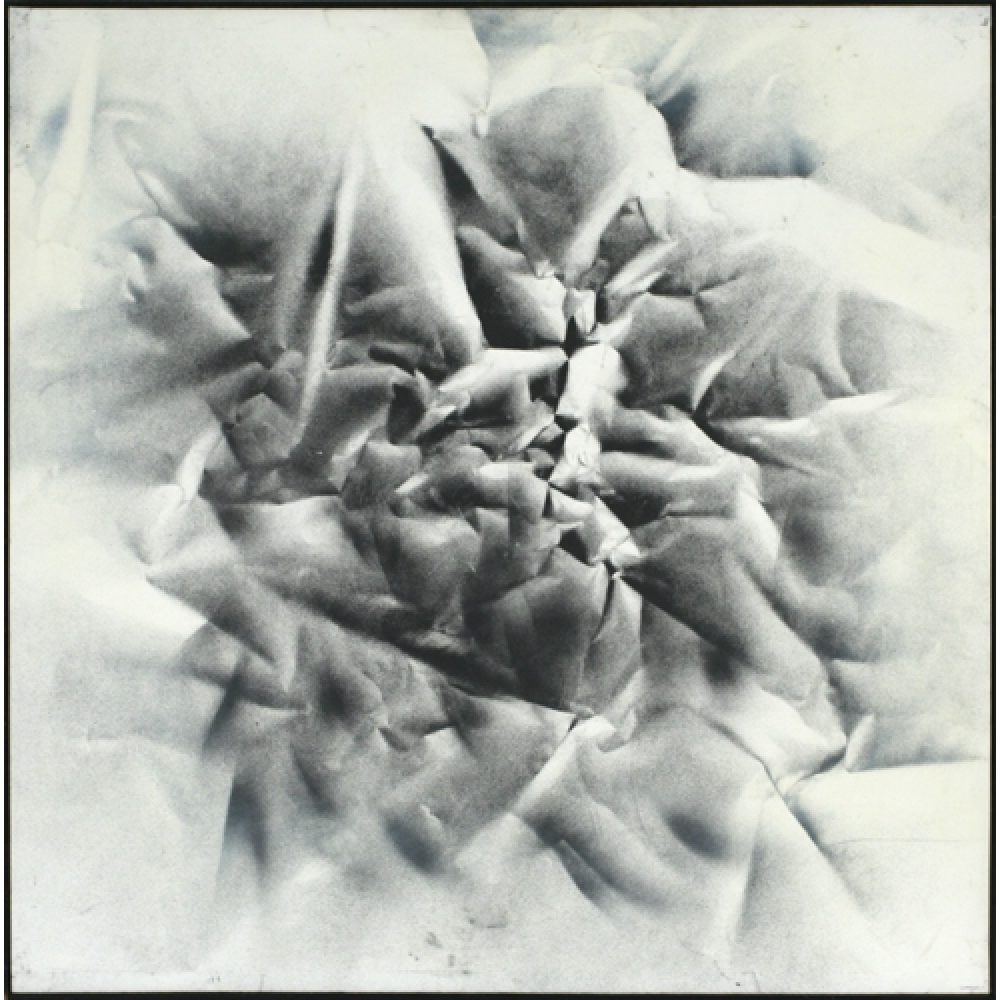 Monochrome artwork with a crumpled texture effect central to the composition. The majority of the composition features a concentrated arrangement of folds and creases, forming a sharp, star-like pattern that fades to a white background.