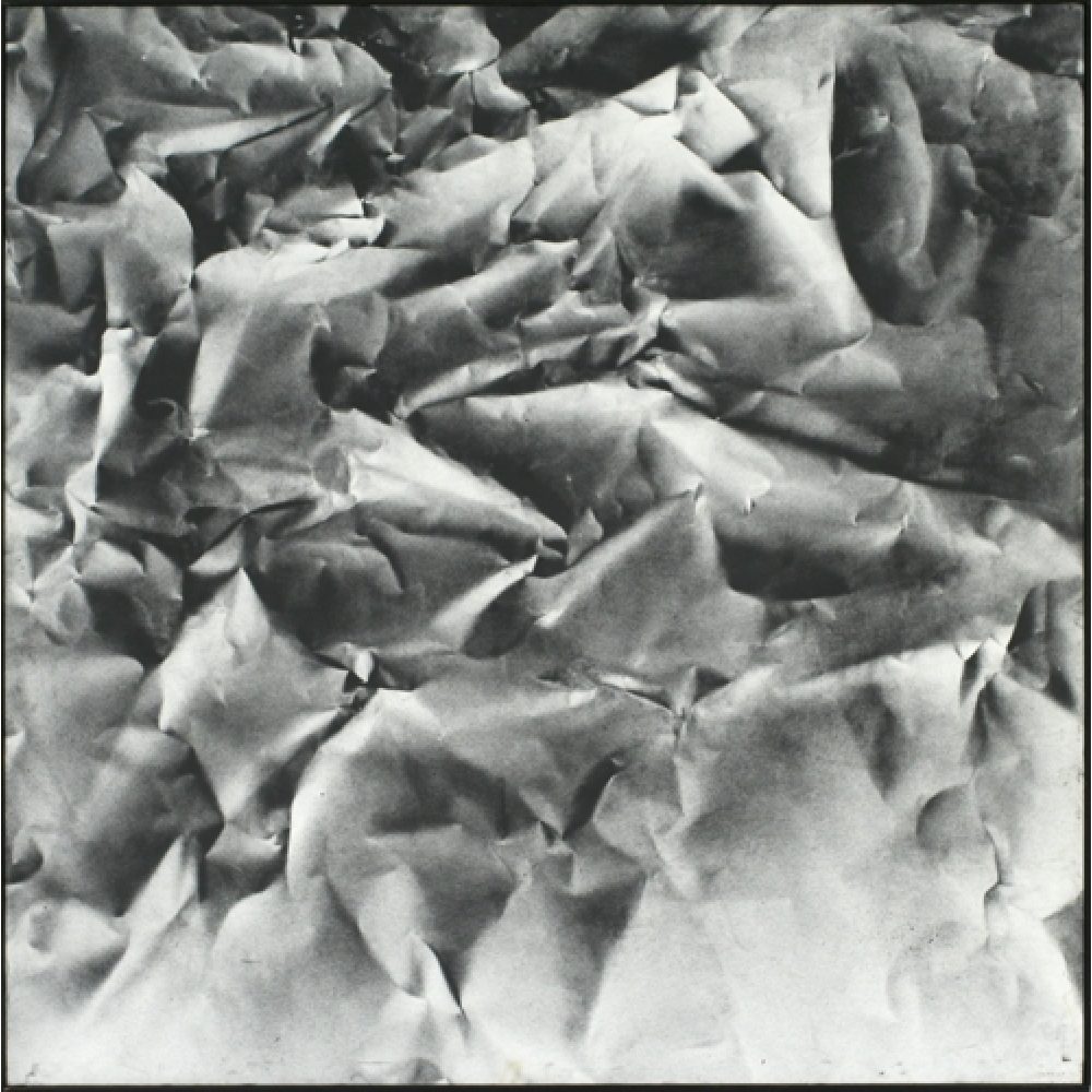 Monochrome artwork composed of a concentrated arrangement of folds and creases, with the painted shapes forming a crumpled paper texture.