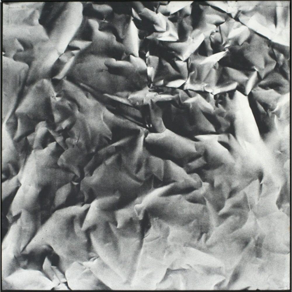 Monochrome artwork composed of a concentrated arrangement of folds and creases, with the painted shapes forming a crumpled paper texture.