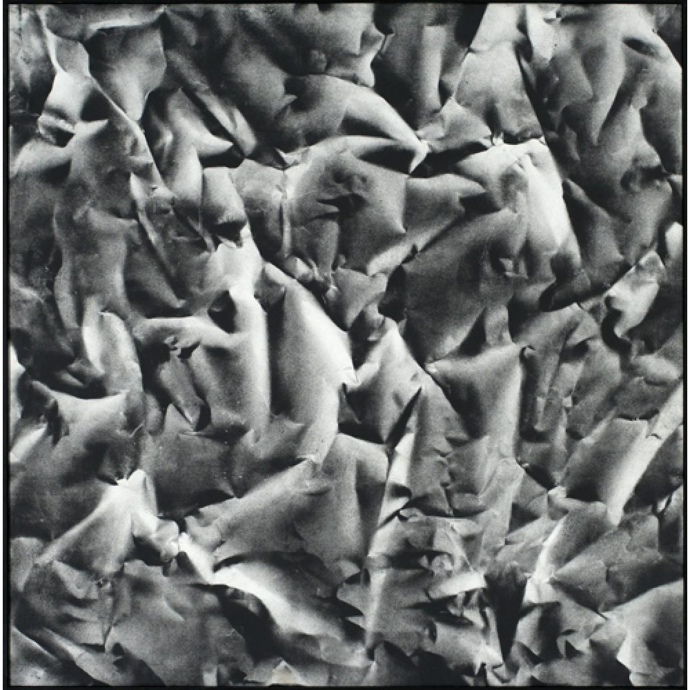 Monochrome artwork composed of a concentrated arrangement of folds and creases, with the painted shapes forming a crumpled paper texture.