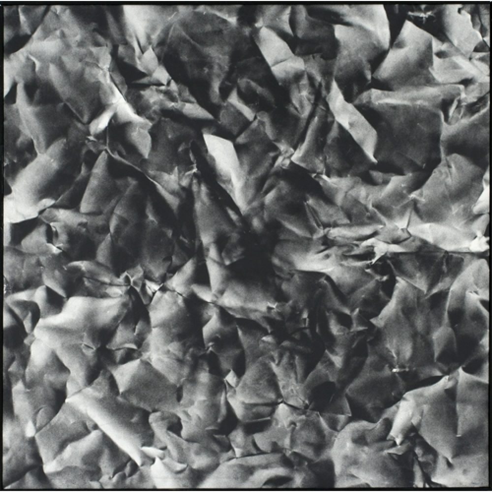 Monochrome artwork composed of a concentrated arrangement of folds and creases, with the painted shapes forming a crumpled paper texture.