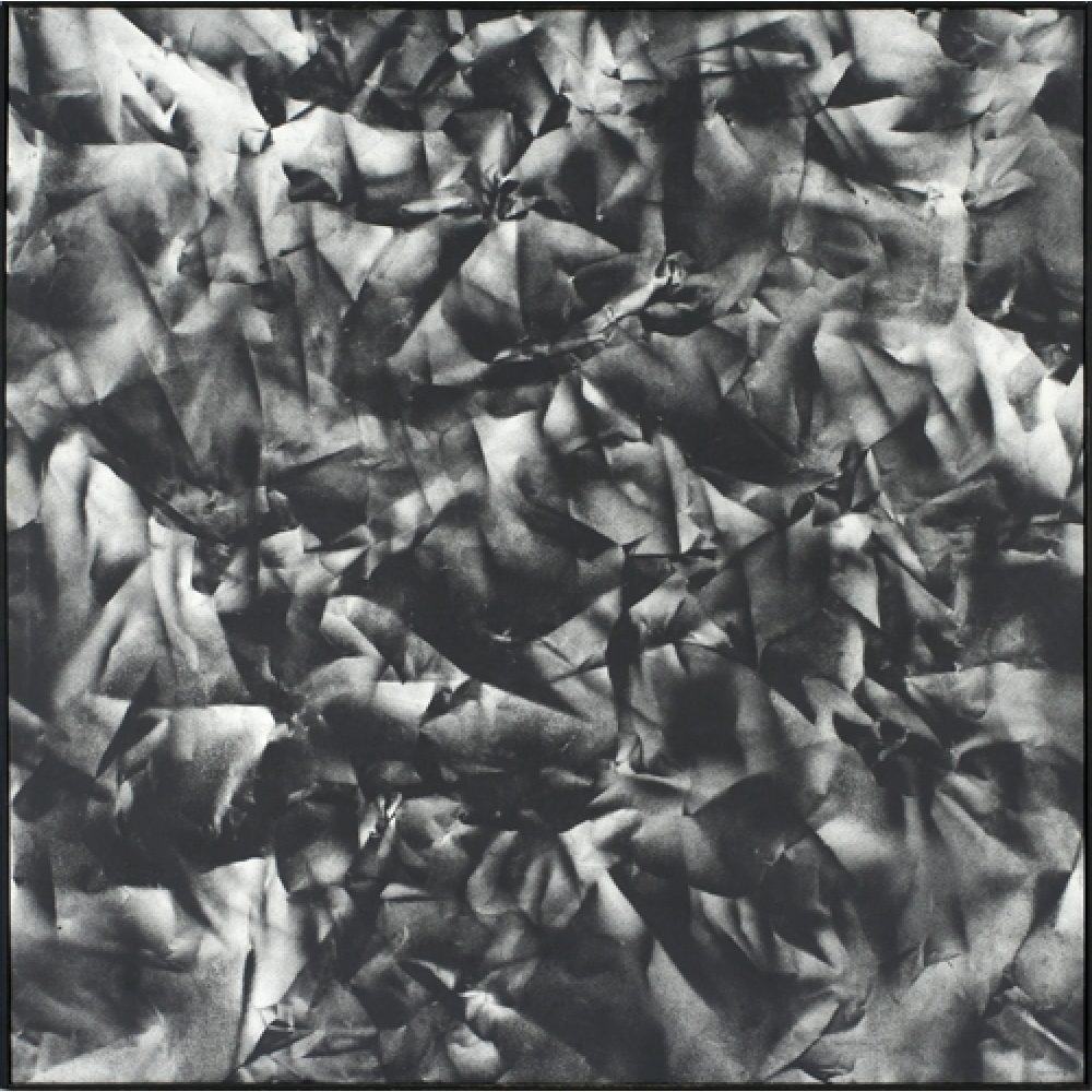Monochrome artwork composed of a concentrated arrangement of folds and creases, with the painted shapes forming a crumpled paper texture.