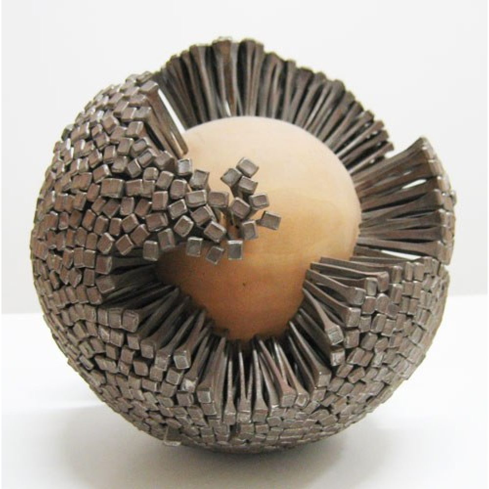 Spherical sculpture composed of a central light wooden ball densely tacked with steel nails; a large area of the wooden orb is not covered with nails and is visible to viewers.
