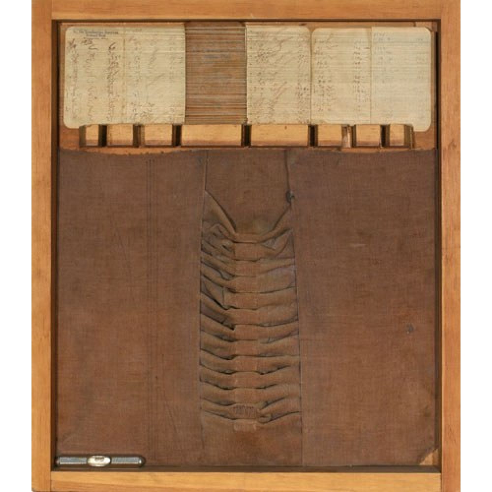 The image features a mixed-media artwork set within a wooden frame. The top section contains a series of overlapping paper cards with faded handwriting, organized neatly at the back of the frame. The middle includes a horizontal section composed of tightly bound thread. Below, there is a large panel of dark brown velvet fabric featuring a series of evenly spaced folds or pleats running vertically down the center. At the bottom of the art piece, a small cylindrical metal object is placed horizontally.