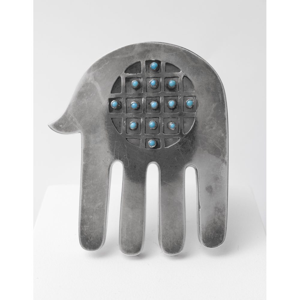 Silver hand-shaped brooch or pendant with turquoise stones in a grid pattern.