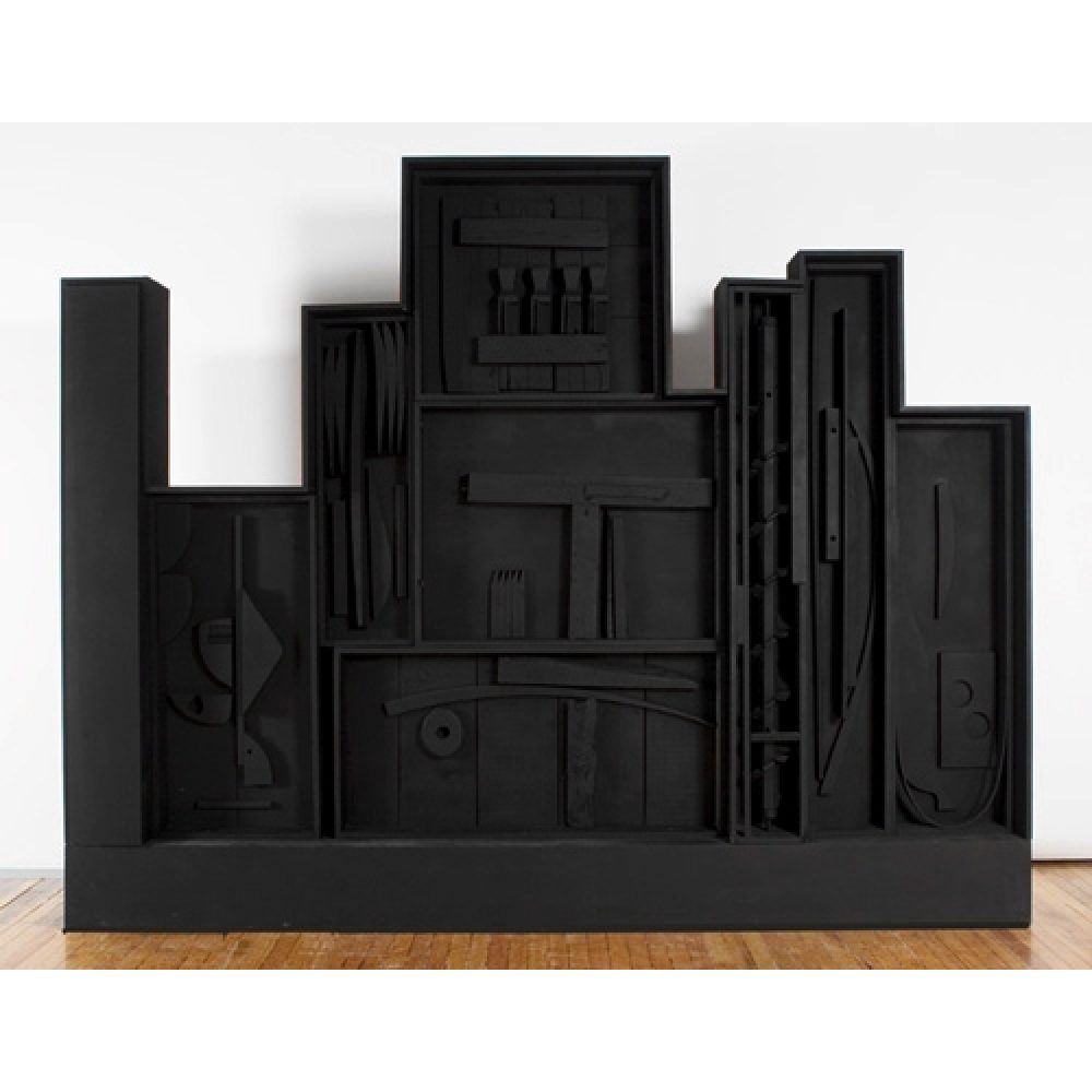 An all black sculpture of various geometric forms arranged in rectangular compartments resembling a city skyline. Alt-text generated by AI.