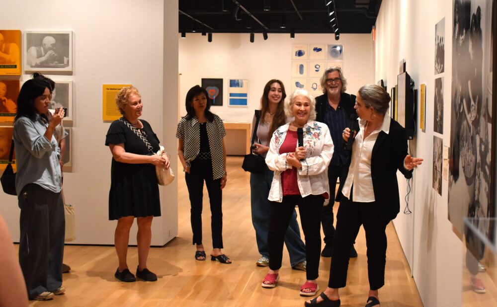 A group of people standing and conversing inside a museum or gallery room. Alt text generated by AI