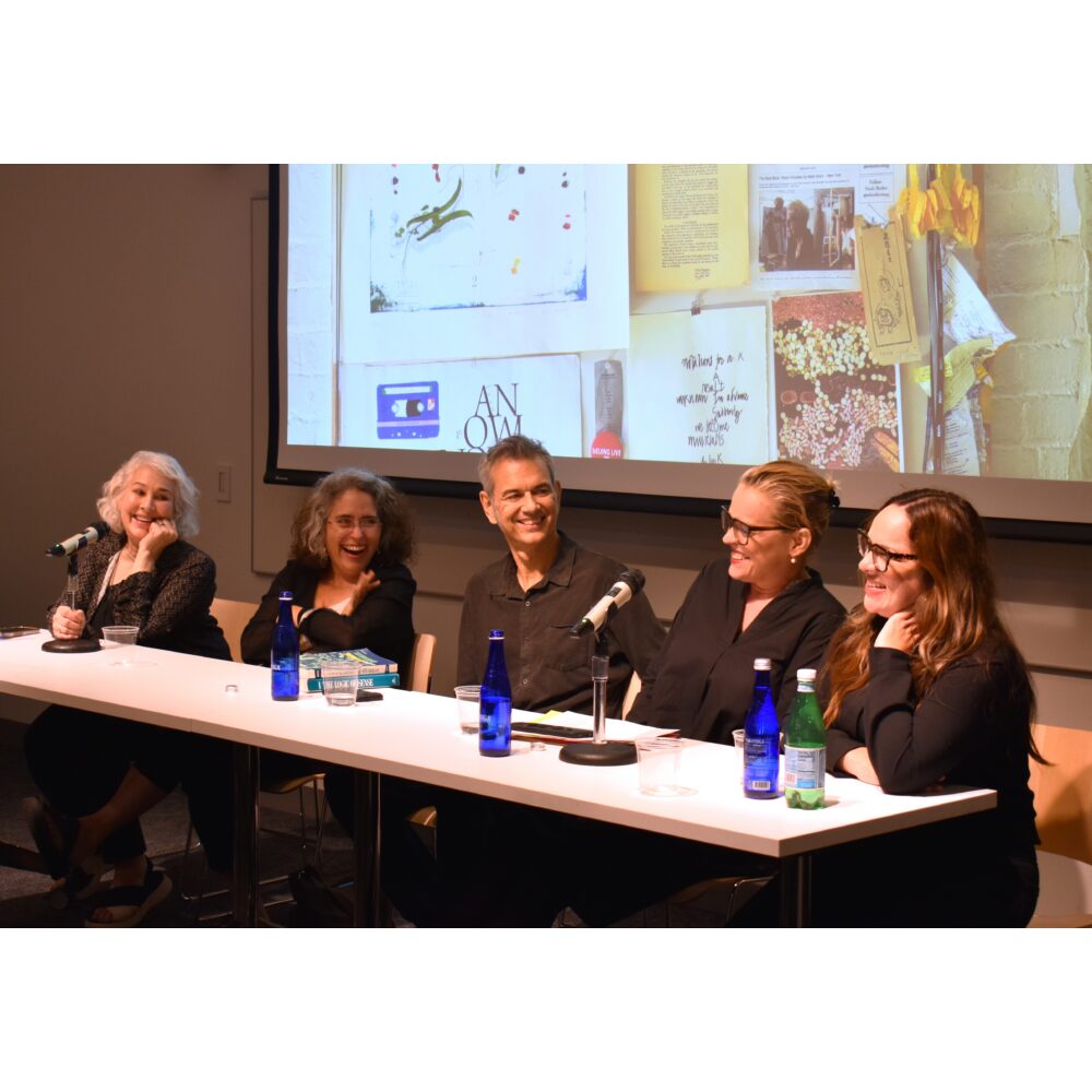 A panel of speakers seated at a long table with microphones during a presentation. Alt text generated by AI