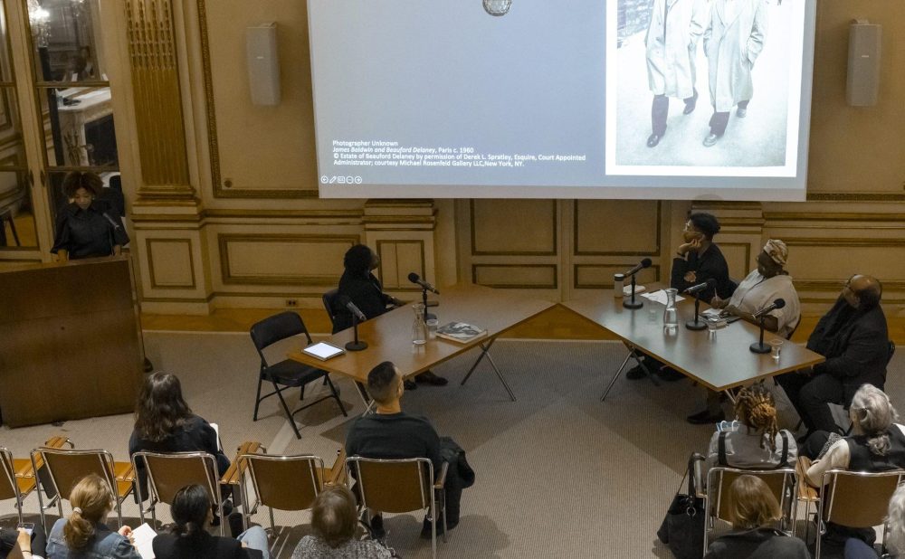 An overhead view of a room full of people looking at a screen and a speaker at a podium to the left of the screen.