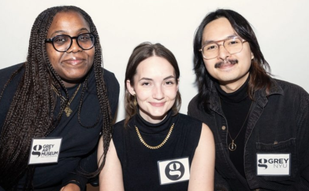Three people sitting together, all wearing black outfits and name tags; at the far left, a black woman with long braids; in the middle, a white brunette women; and at right, an olive-skinned man with shoulder-length hair and a mustache