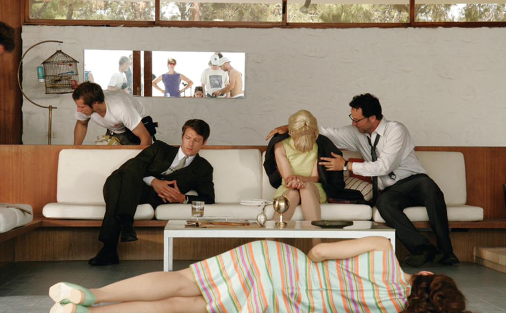 Indoor scene showing people on a couch and a woman lying on the floor in a colorful striped dress.