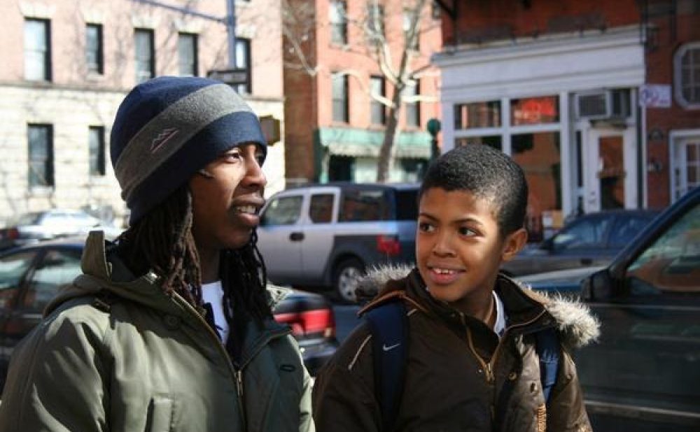 Two boys, one older, one younger, looking at each other and talking while walking down the street