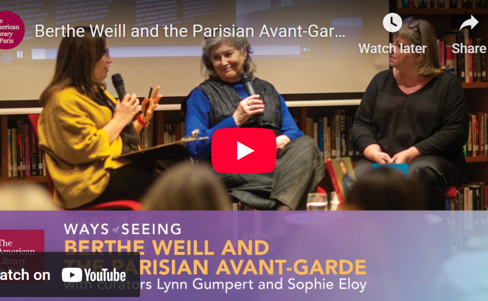 Three women having a discussion on a stage with microphones, with a YouTube play button overlay.