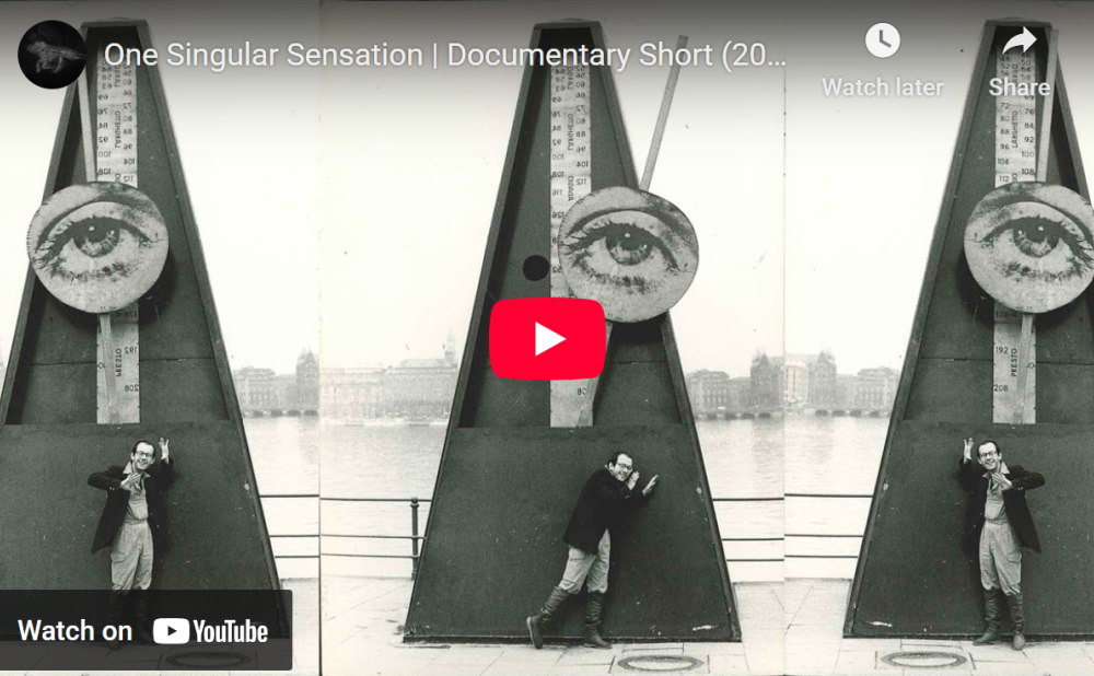 A YouTube video thumbnail featuring three images of a person beside a large, triangular metronome structure with an eye illustration at the top, set near a body of water.