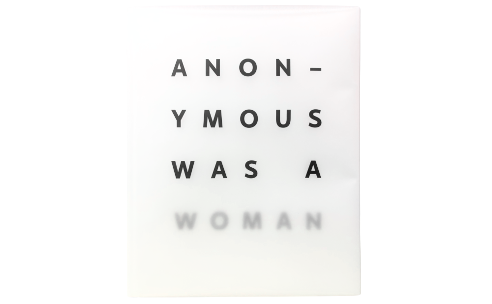 A book titled Anonymous WAs A Woman: The First 25 Years lays closed on a table; its front cover bears the title, the word "woman" blurred by the transparent dust jacket.
