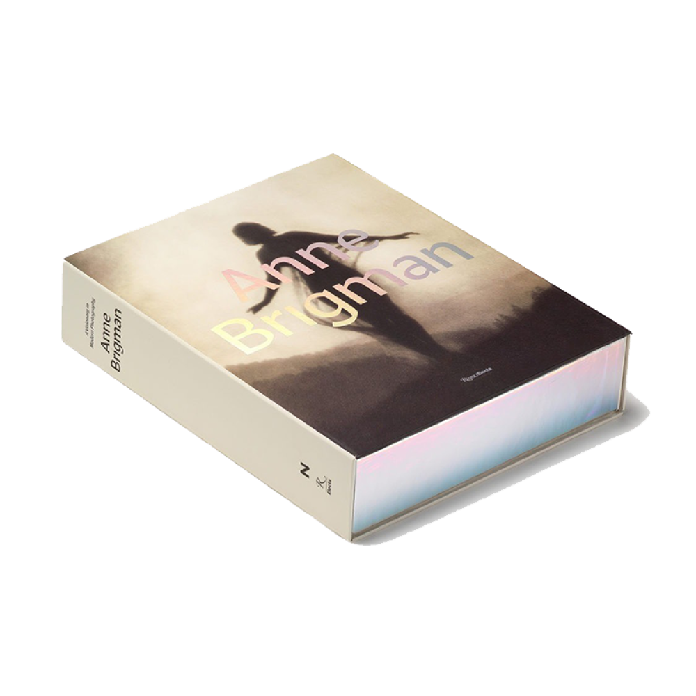 Three-quarter view of a book laying on a flat surface, cover up, titled "Anne Brigman" with a silhouette on the cover and a colorful sheen on the fore-edge.