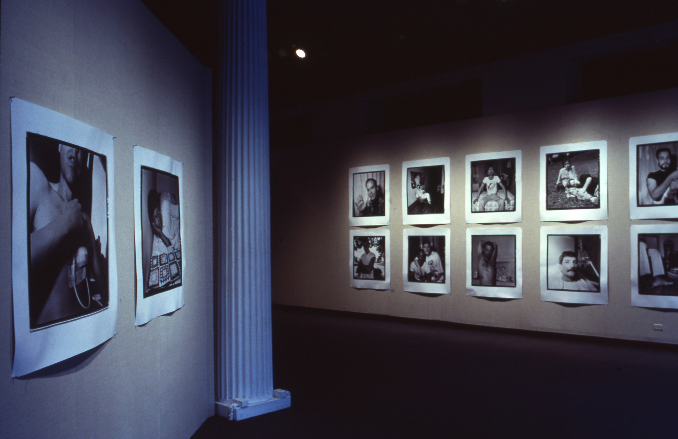 Art gallery exhibition with black-and-white photographs on beige walls, divided by a white column. Alt-text generated by AI.