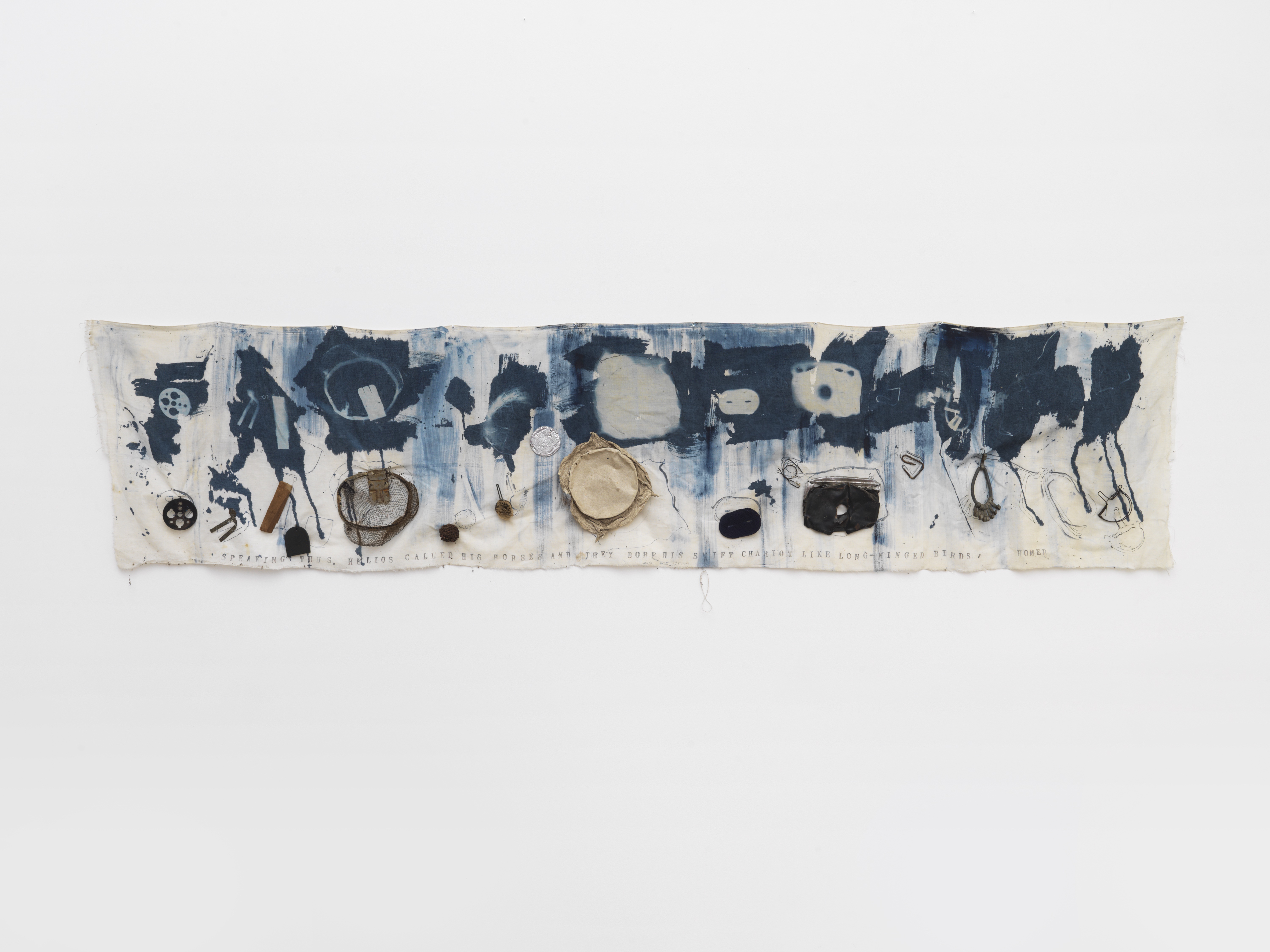 Abstract printed cloth artwork with blue ink patterns and attached objects, hanging on a white background. Alt-text generated by AI.