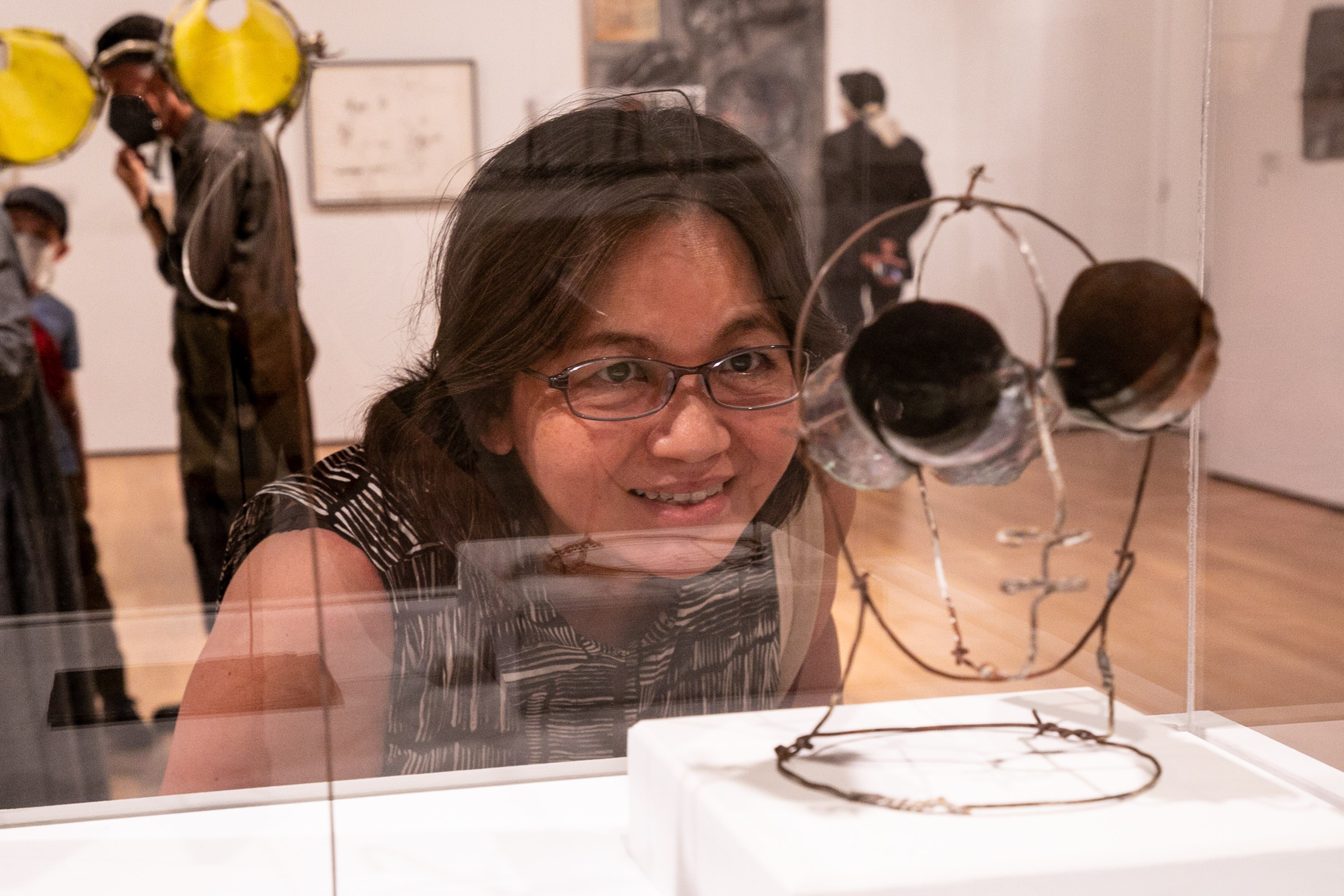 A woman with glasses smiles while looking at a wire sculpture in an art gallery. Alt-text generated by AI.
